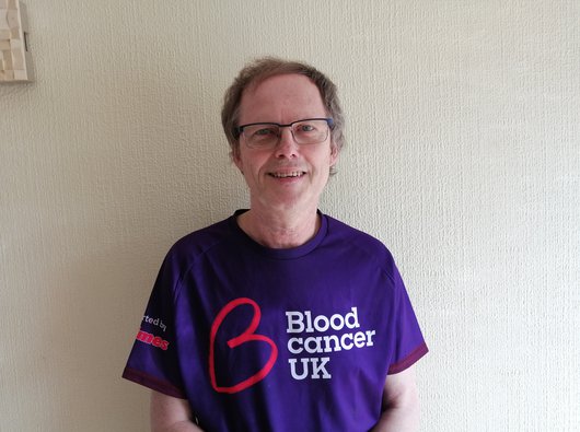 David, who is living with CLL, looks to camera and smiles. He is wearing a Blood Cancer UK t-shirt.
