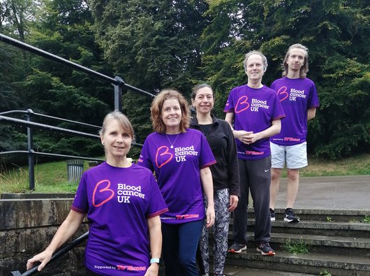 A group of five people pose together on steps outside; they wear purple Blood Cancer UK T shirts.