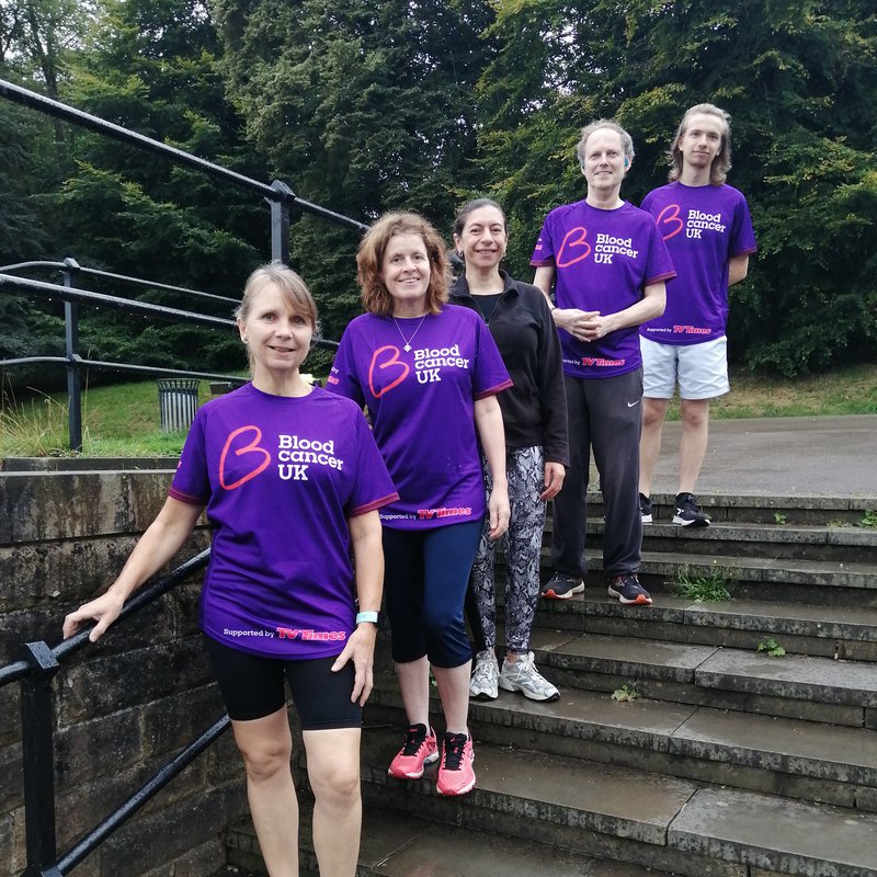 A group of five people pose together on steps outside; they wear purple Blood Cancer UK T shirts.