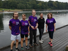 A group of five people pose together on decking next to a river; they wear purple Blood Cancer UK T shirts.