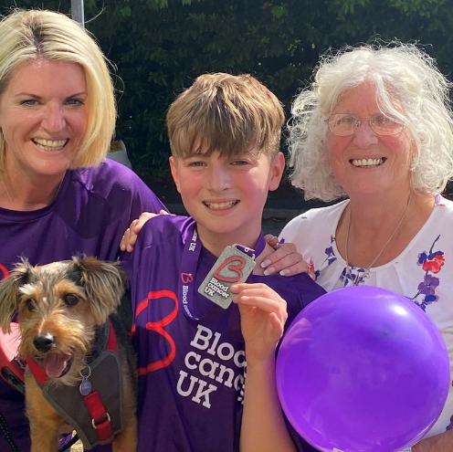 A young boy poses with a Blood Cancer UK medal, flanked by his mother and grandmother.