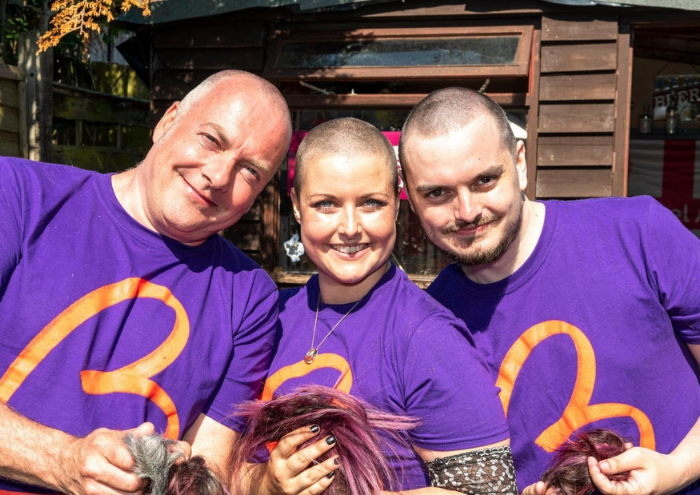 A woman - Jemma - shares a moment with two men. They all wear purple Blood Cancer UK T shirts.
