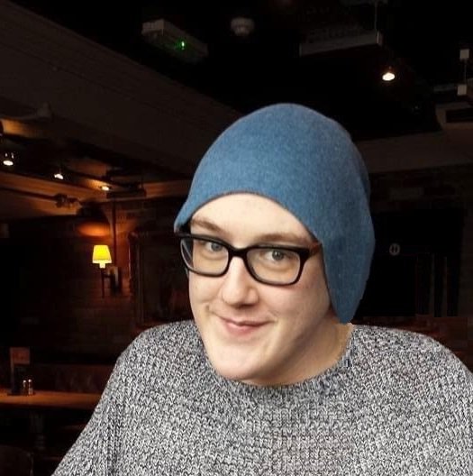 Josh sitting in a bar smiling, wearing a hat and a jumper.