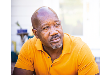 An older middle aged Black man in a yellow shirt.