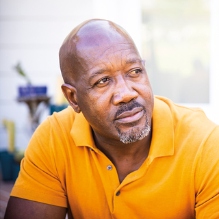 An older middle aged Black man in a yellow shirt.
