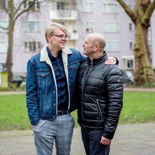 A male couple share a tender moment in a housing estate garden.