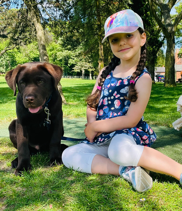 A young child Mia sits in a park next to her puppy dog.
