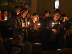 A group of people sing Christmas carols in a dark, candlelit room