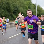 A runner waves at the camera during a marathon; he wears a Blood Cancer UK T-shirt.