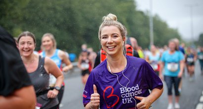 A runner smiles as she runs a marathon; she wear a Blood Cancer UK t shirt.