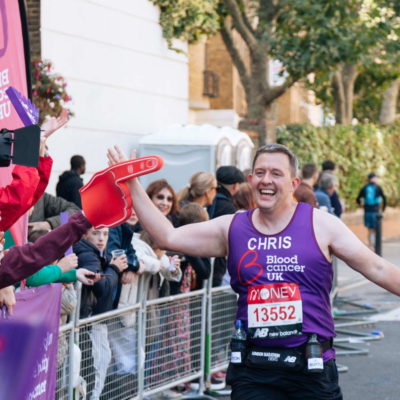 A runner high fives a supporter during a marathon. He wears a Blood Cancer UK T shirt.