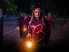 A woman wearing a Blood Cancer UK t-shirt leads a night time walk, holding a lantern, looking calm and happy.