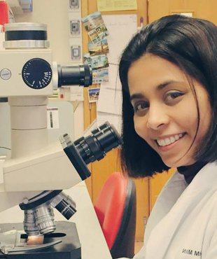 Anndita Roy - a researcher -  in a lab looking directly at the camera with a microscope